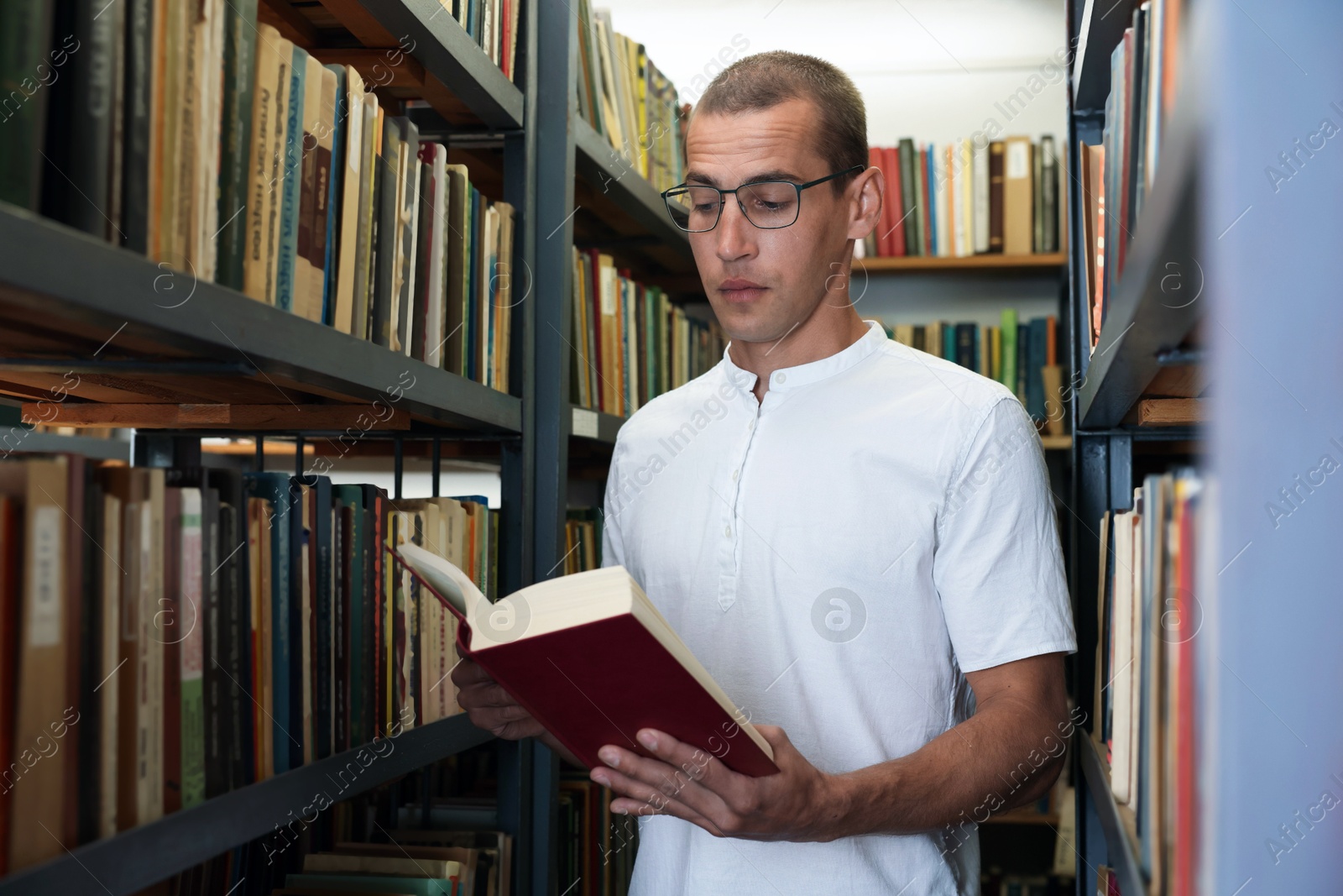 Photo of Man reading book near shelves in public library