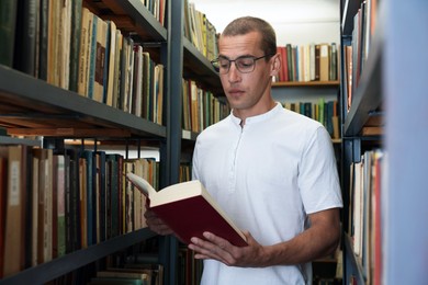 Photo of Man reading book near shelves in public library