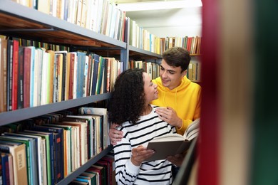 Photo of Students studying together near shelves with books in public library