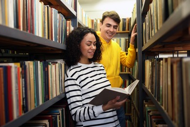 Photo of Students studying together near shelves with books in public library