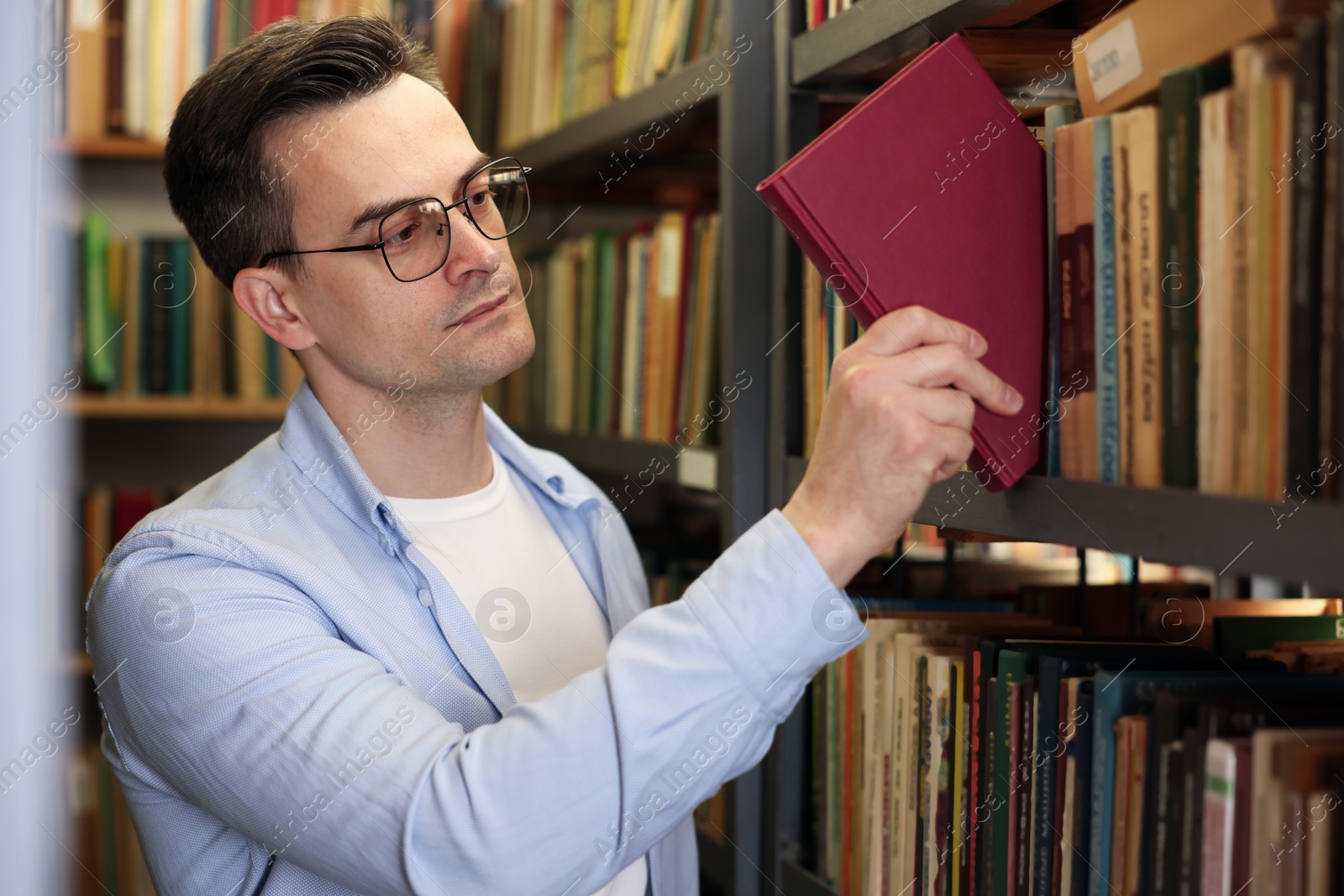 Photo of Man taking book from shelf in public library