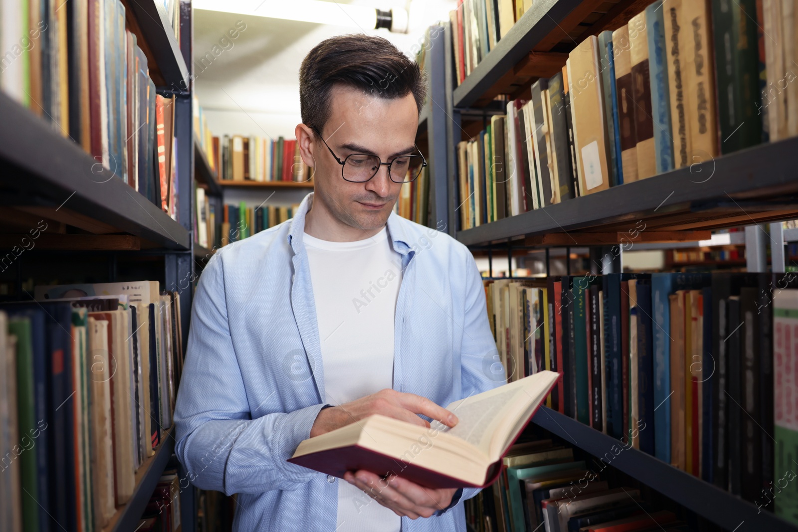 Man reading book near shelves in public library Photo of Man reading book near shelves in public library