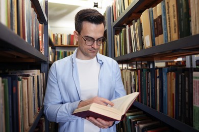 Photo of Man reading book near shelves in public library