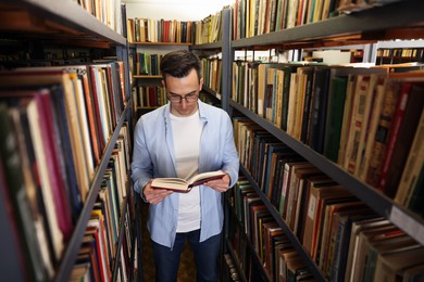 Photo of Man reading book near shelves in public library