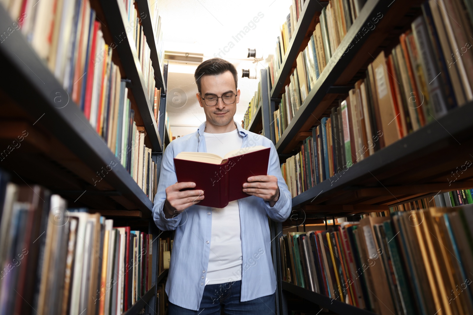 Photo of Man reading book near shelves in public library, low angle view