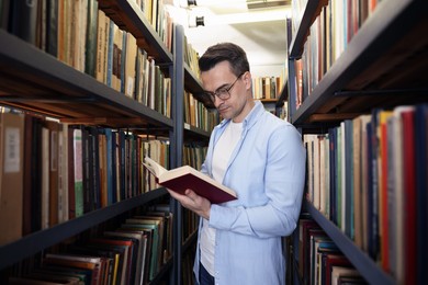 Photo of Man reading book near shelves in public library