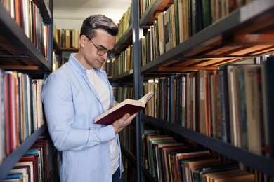 Photo of Man reading book near shelves in public library