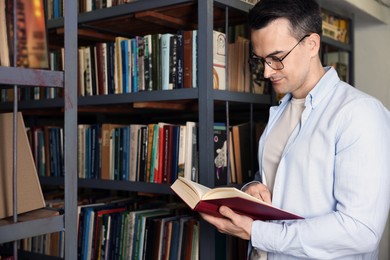 Photo of Man reading book near shelves in public library