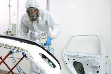 Photo of Worker spray painting car in body shop
