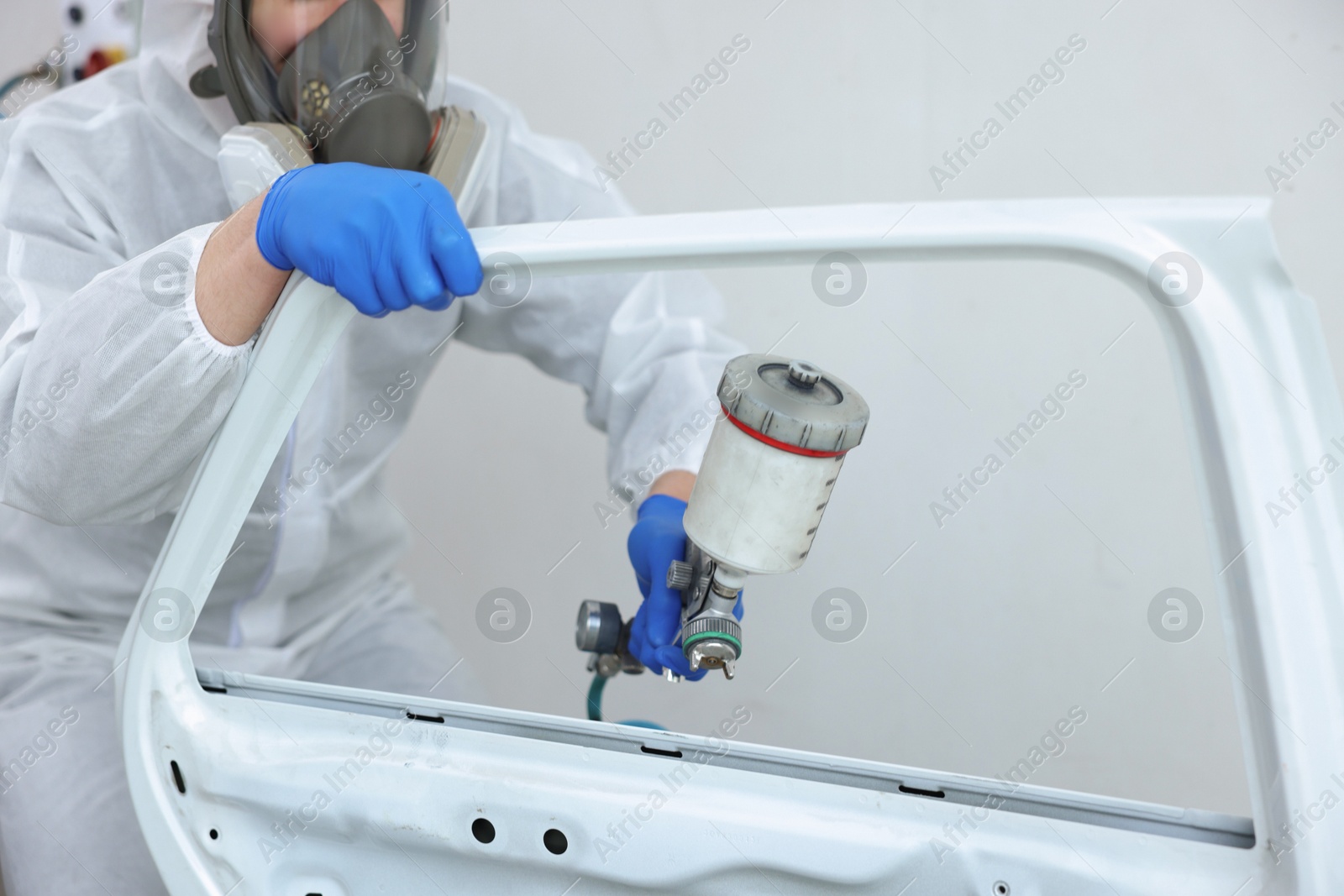 Photo of Worker painting car door in body shop, closeup
