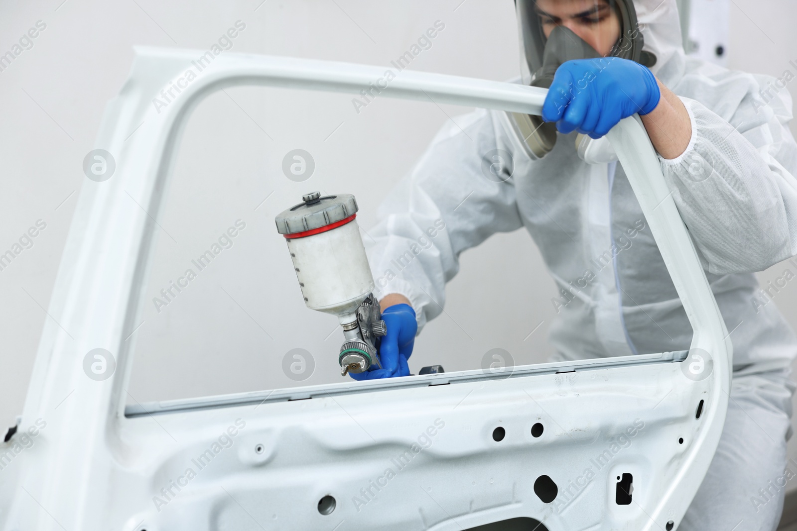 Photo of Worker painting car door in body shop, closeup