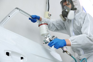 Photo of Worker painting car door in body shop, selective focus