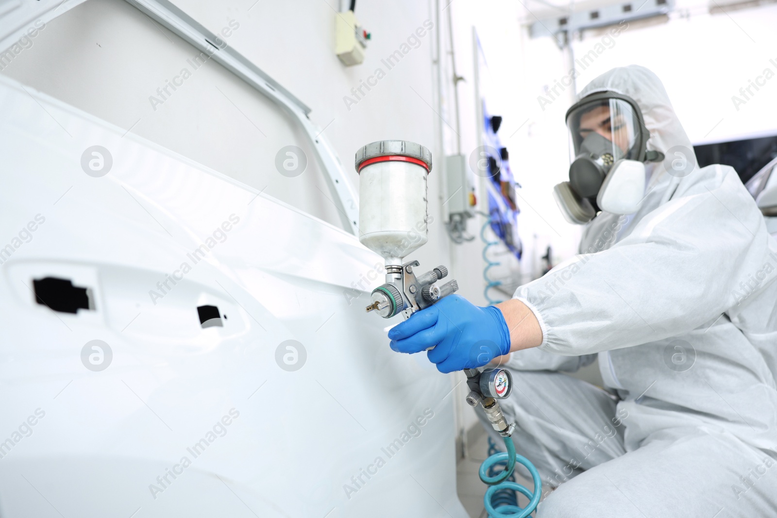 Photo of Worker painting car door in body shop, selective focus