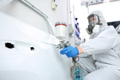 Photo of Worker painting car door in body shop, selective focus