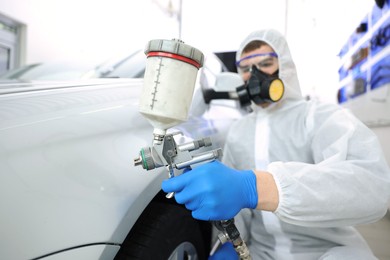 Photo of Worker painting car in body shop, selective focus
