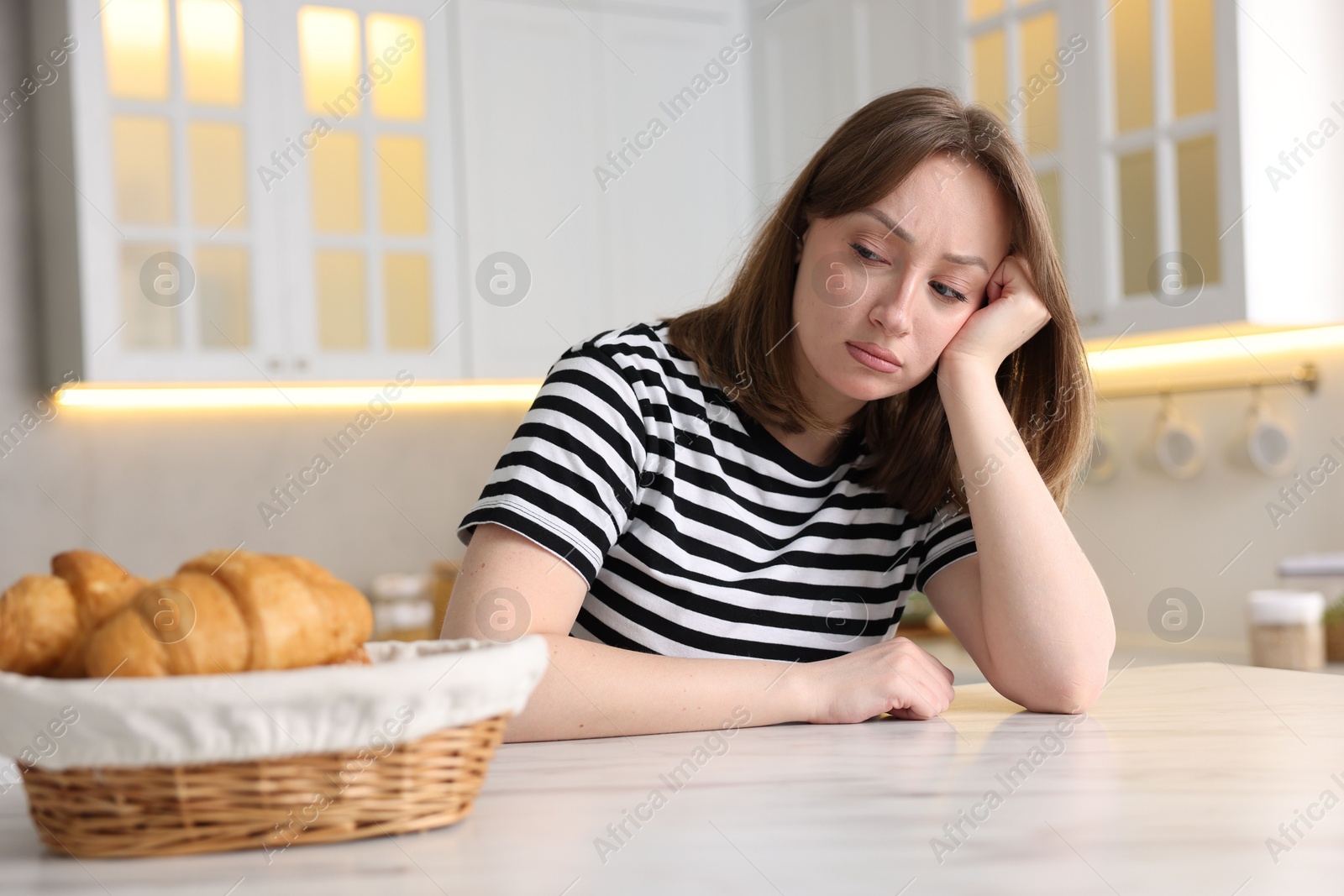 Gluten free diet. Sad woman looking at croissants at white marble table in kitchen Photo of Gluten free diet. Sad woman looking at croissants at white marble table in kitchen
