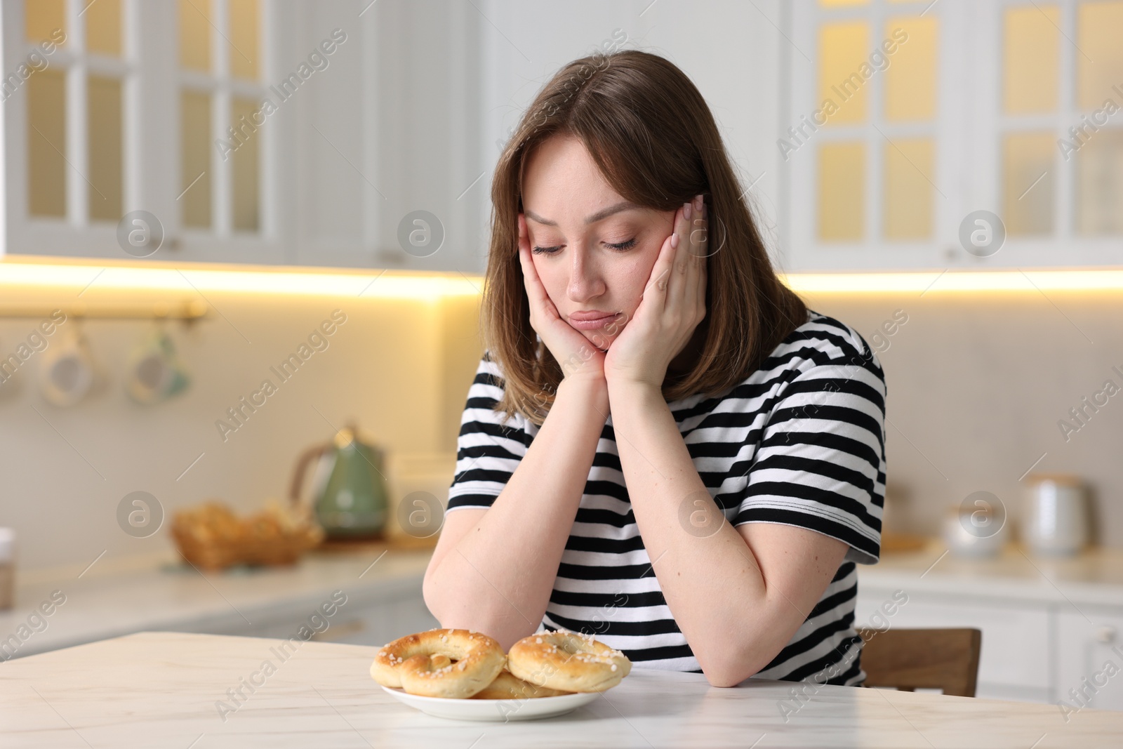 Gluten free diet. Sad woman with pretzels at white marble table in kitchen, space for text Photo of Gluten free diet. Sad woman with pretzels at white marble table in kitchen, space for text