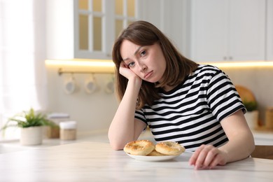 Photo of Gluten free diet. Sad woman with pretzels at white marble table in kitchen, space for text