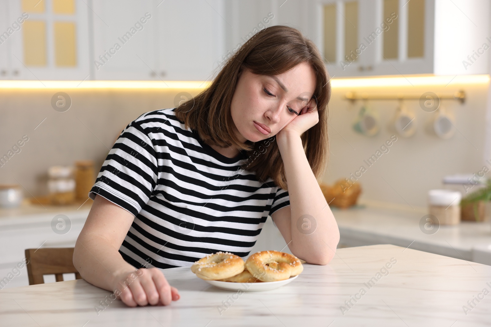 Gluten free diet. Sad woman with pretzels at white marble table in kitchen, space for text Photo of Gluten free diet. Sad woman with pretzels at white marble table in kitchen, space for text