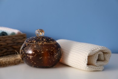 Photo of Clean waffle towel and jar of product on white dresser near blue wall, closeup