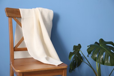 Photo of Clean waffle towel on chair and houseplant near blue wall