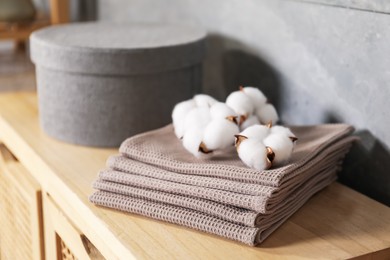 Photo of Clean waffle towels and cotton flowers on wooden dresser in bathroom, closeup