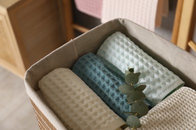Photo of Clean waffle towels and branch in basket indoors, closeup