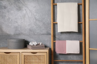 Photo of Clean waffle towels, wooden rack and dresser near grey wall in bathroom