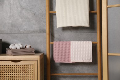 Photo of Clean waffle towels, wooden rack and dresser near grey wall in bathroom