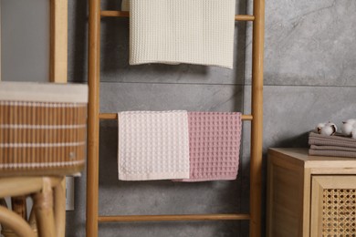 Photo of Clean waffle towels, wooden rack and dresser near grey wall in bathroom