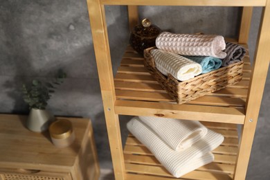 Photo of Clean waffle towels on wooden shelving unit near grey wall in bathroom, closeup