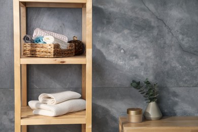 Photo of Clean waffle towels on wooden shelving unit near grey wall in bathroom