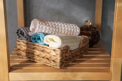 Photo of Clean waffle towels on wooden shelving unit near grey wall in bathroom, closeup