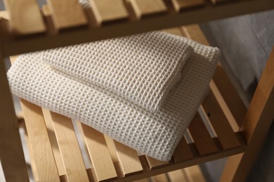 Photo of Clean waffle towels on wooden shelving unit near grey wall in bathroom, closeup