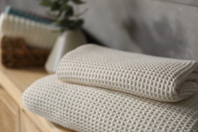 Photo of Clean waffle towels on wooden dresser near grey wall in bathroom, closeup