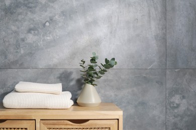 Photo of Waffle towels and vase with branches on wooden dresser near grey wall, space for text