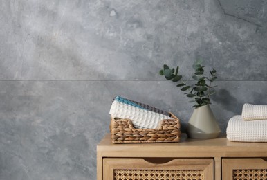 Photo of Waffle towels and vase with branches on wooden dresser near grey wall, space for text
