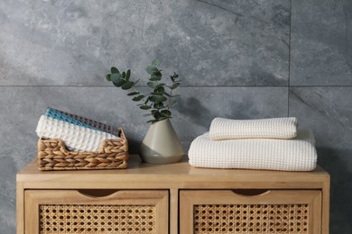 Photo of Waffle towels and vase with branches on wooden dresser near grey wall