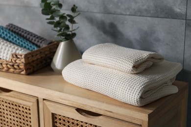 Photo of Waffle towels and vase with branches on wooden dresser near grey wall