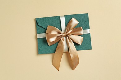Photo of Envelope with golden bow on beige background, top view