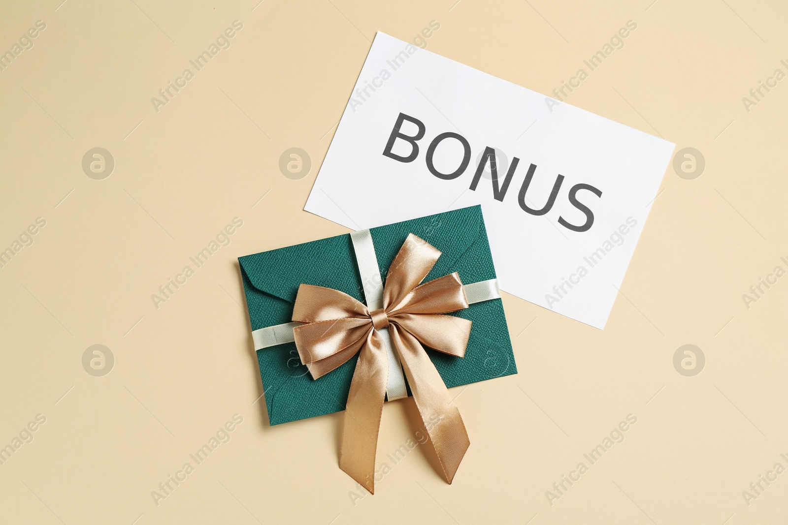 Envelope with golden bow and card with word Bonus on beige background, flat lay Photo of Envelope with golden bow and card with word Bonus on beige background, flat lay