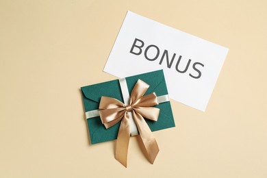 Photo of Envelope with golden bow and card with word Bonus on beige background, flat lay