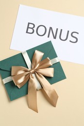 Photo of Envelope with golden bow and card with word Bonus on beige background, flat lay