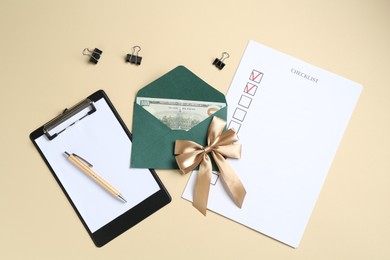 Photo of Money bonus. Envelope with dollar banknote, clipboard, checklist and binder clips on beige background, flat lay
