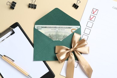 Photo of Money bonus. Envelope with dollar banknote, clipboard, checklist and binder clips on beige background, flat lay