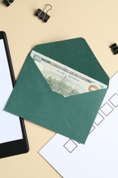 Photo of Money bonus. Envelope with dollar banknote, clipboard, checklist and binder clips on beige background, flat lay