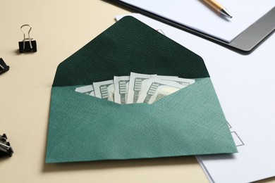 Photo of Money bonus. Envelope with dollar banknotes, clipboard and binder clips on beige background, closeup