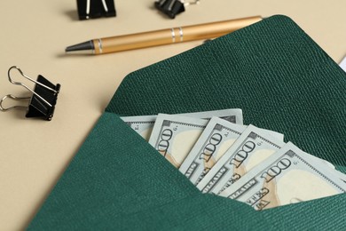 Photo of Money bonus. Envelope with dollar banknotes, pen and binder clips on beige background, closeup