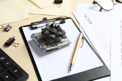 Photo of Money bonus. Dollar banknotes with bow, stationery, calculator and checklists on beige background, closeup