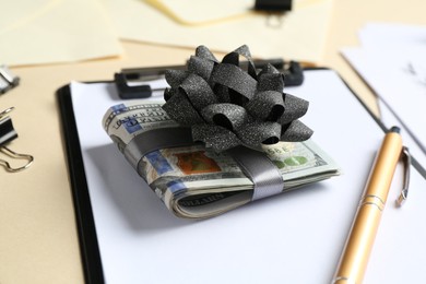 Photo of Money bonus. Dollar banknotes with bow, pen and clipboard on beige background, closeup